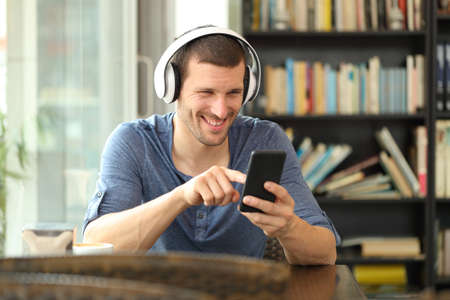 Happy man listening to music with headphones and smart phone sitting in a coffee shopの写真素材