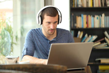 Adult man wearing headphones using a laptop e-learning in a coffee shop or homeの写真素材