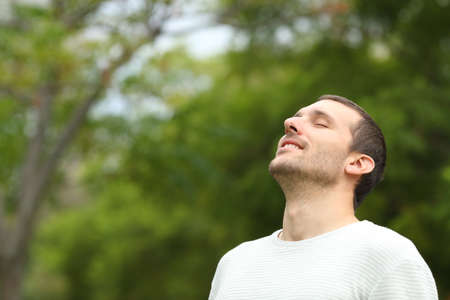 Happy man breathing deeply fresh air in a forest with green trees in the backgroundの写真素材