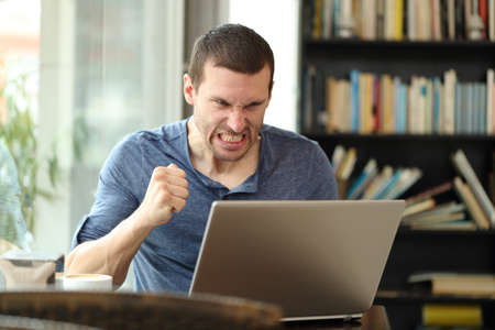 Angry adult man checking laptop online content sitting in a bar or homeの写真素材