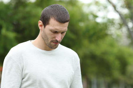 Sad man walking alone looking down complaining in a parkの写真素材