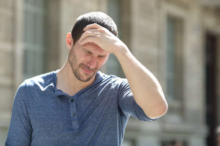 Stressed adult man complaining suffering headache touching head in the streetの写真素材