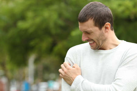 Man suffering itching cratching arm standing in a parkの写真素材