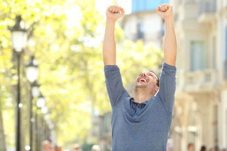 Excited man raising arms celebrating success in the street of a big cityの写真素材