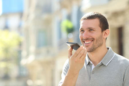 Happy man using voice recognition on mobile phone to send a recorded message in the streetの写真素材