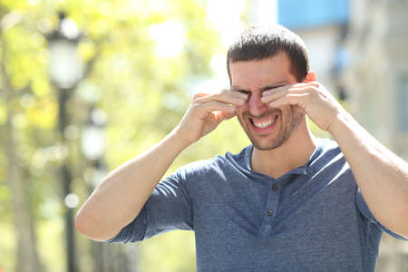 Adult man scratching itchy eyes with both hands standing in the streetの写真素材