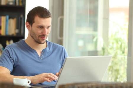 Serious adult man using a laptop browsing web sitting in a coffee shop or homeの写真素材