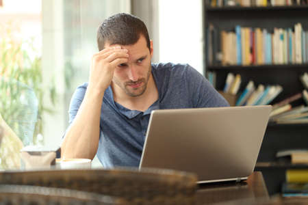 Worried adult man checking laptop online content sitting in a coffee shopの写真素材