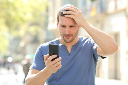 Confused man complaining after mistake checking mobile phone content in the streetの写真素材