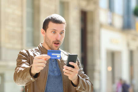 Surprised man paying on line with credit card and mobile phone in the streetの写真素材