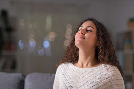 Relaxed arab woman breathing fresh air sitting on a couch in the living room in the night at homeの写真素材