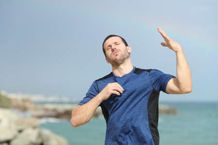 Stressed runner suffering heat stroke complaining and fanning with his hand on the beachの写真素材