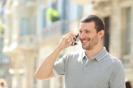 Happy adult man talking on mobile phone walking in the streetの写真素材