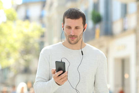 Front view portrait of a serious adult man listening to music on phone wearing earbuds in the streetの写真素材