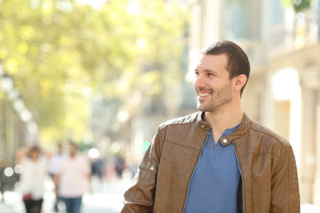 Front view of a happy man walking towards camera in the street looking at sideの写真素材