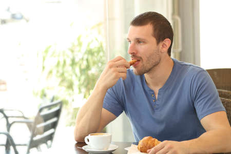 Relaxed man eating a croissant for breakfast sitting in a coffee shopの写真素材