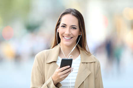Front view portrait of a happy woman listening to music looks at camera in the streetの写真素材