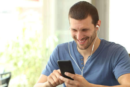 Happy man listening to music using smart phone sitting in a coffee shop or homeの写真素材