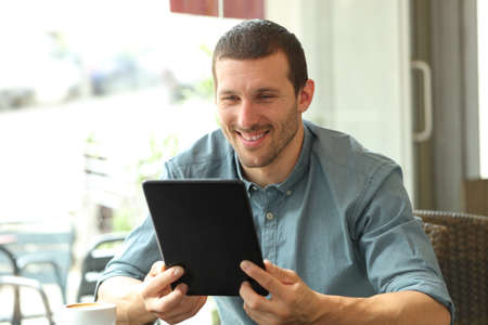 Happy man reading tablet content sitting in a coffee shopの写真素材