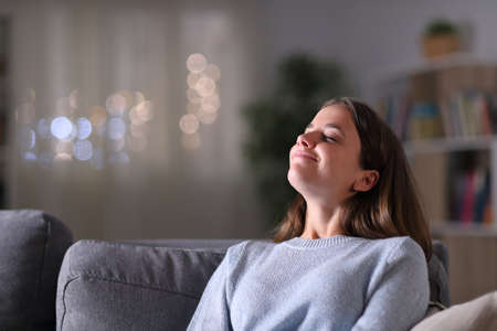 Relaxed homeowner breathing deeply fresh air sitting on a couch in the living room in the night at homeの写真素材