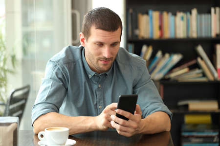Relaxed man using a smart phone to browse online content sitting in a coffee shopの写真素材