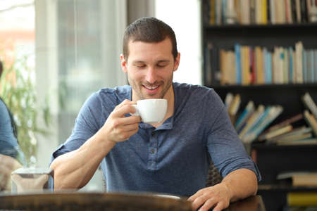 Front view of a happy man enjoying a cup of coffee sitting in a barの写真素材
