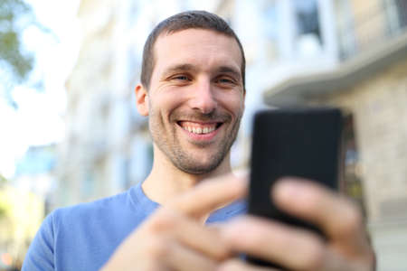 Close up of a happy adult man browsing mobile phone content in the streetの写真素材