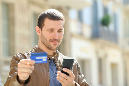 Serious man paying on line with credit card and mobile phone standing in the streetの写真素材