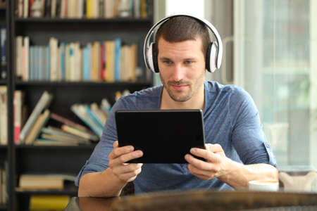 Serious man using tablet and headphones to watch online media sitting in a coffee shopの写真素材