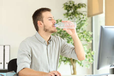 Office worker working and drinking bottled water sitting on a chair at workplaceの写真素材