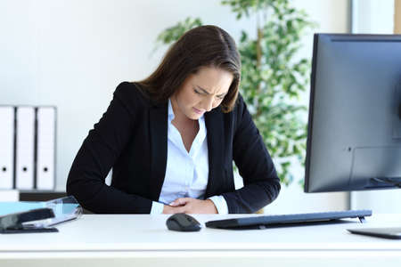 Young businesswoman suffering bellyache working sitting at officeの写真素材