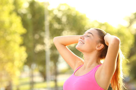Happy sportswoman breathing fresh air standing in a park ar sunsetの写真素材