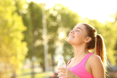 Happy sportswoman holding water bottle breathing fresh air in a parkの写真素材