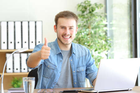 Front view portrait of a happy entrepreneur gesturing thumbs up at officeの写真素材