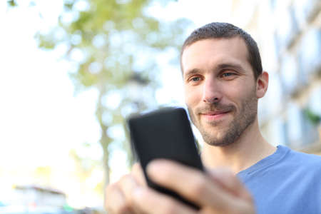 Close up of a satisfied man using smart phone walking in the streetの写真素材