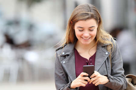 Front view portrait of a happy girl texting on mobile phone in the street with copy space at sideの写真素材
