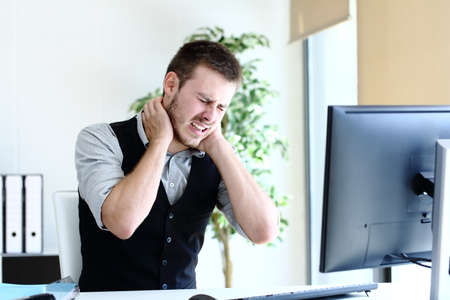 Young executive man suffering neck ache working sitting at officeの写真素材