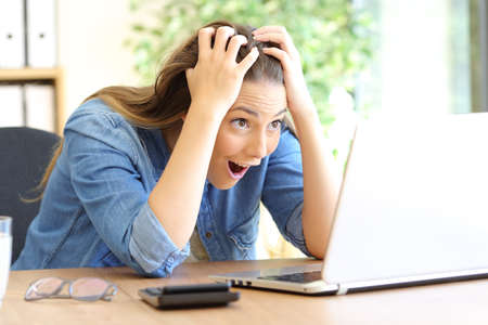 Amazed businesswoman finding online surprising content on laptop at officeの写真素材