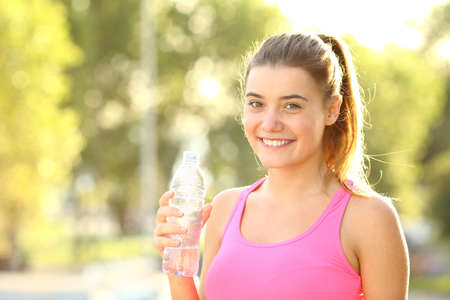 Happy runner looks at camera holding a water bottle standing in a parkの写真素材