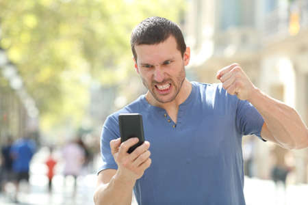 Front view portrait of an angry man checking crashed smart phone standing in the streetの写真素材