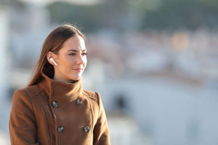 Relaxed woman listening to music using wireless earphones looking away in winterの写真素材