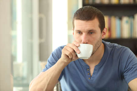 Distracted adult man drinking coffee sitting in a bar or homeの写真素材