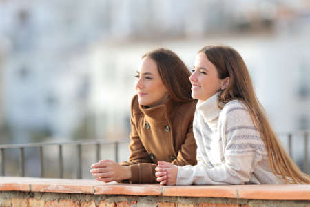 Two relaxed friends contemplating views from a balcony in winter in a rural townの写真素材