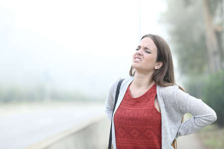 Woman suffering backache standing a foggy cold day in a parkの写真素材