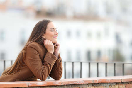 Side view portrait of a satisfied woman wearing jacket heating in winter with closed eyes in a balconyの写真素材