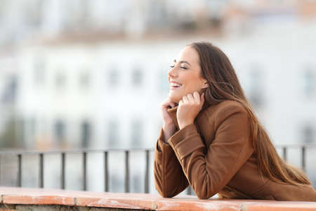 Happy woman heating grabbing jacket in a balcony in winterの写真素材