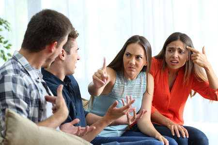 Two angry men and women arguing sitting on a couch in the living room at homeの写真素材