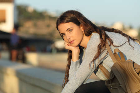 Serious casual girl looks at you at sunset sitting in the streetの写真素材
