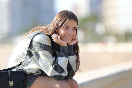 Portrait of a happy girl sitting and looking at camera in winter in the streetの写真素材