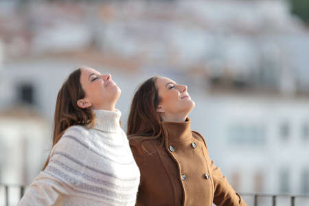 Two relaxed women breathing deeply fresh air in a balcony in winterの写真素材
